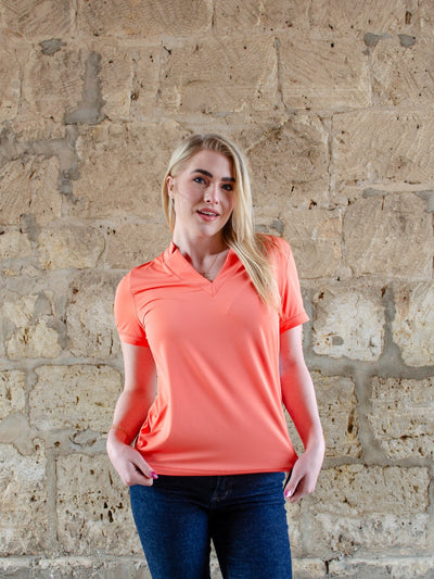 Model is wearing a orange colored collared athletic short sleeve t-shirt. T-shirt worn with jeans.