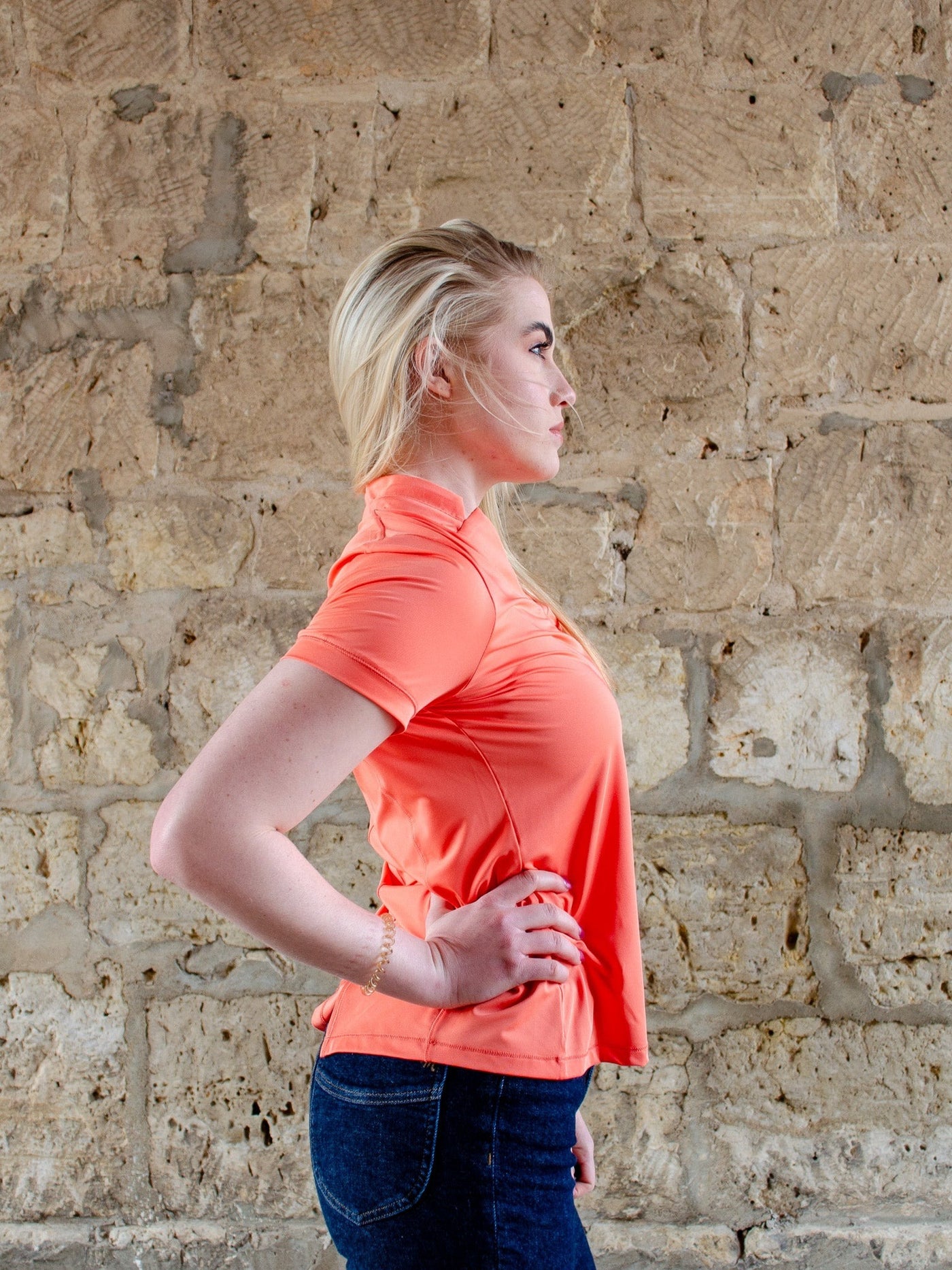 Model is wearing a orange colored collared athletic short sleeve t-shirt. T-shirt worn with jeans