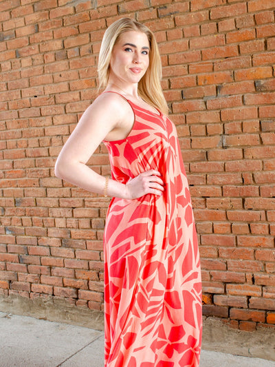 Model is wearing a beachy style orange printed maxi dress. Dress is worn with sneakers.