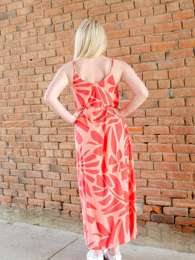 Model is wearing a beachy style orange printed maxi dress. Dress is worn with sneakers.