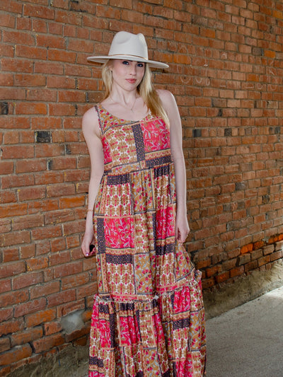 Model is wearing a multi colored patchwork print style maxi dress. Dress is paired with a flat brim hat. 