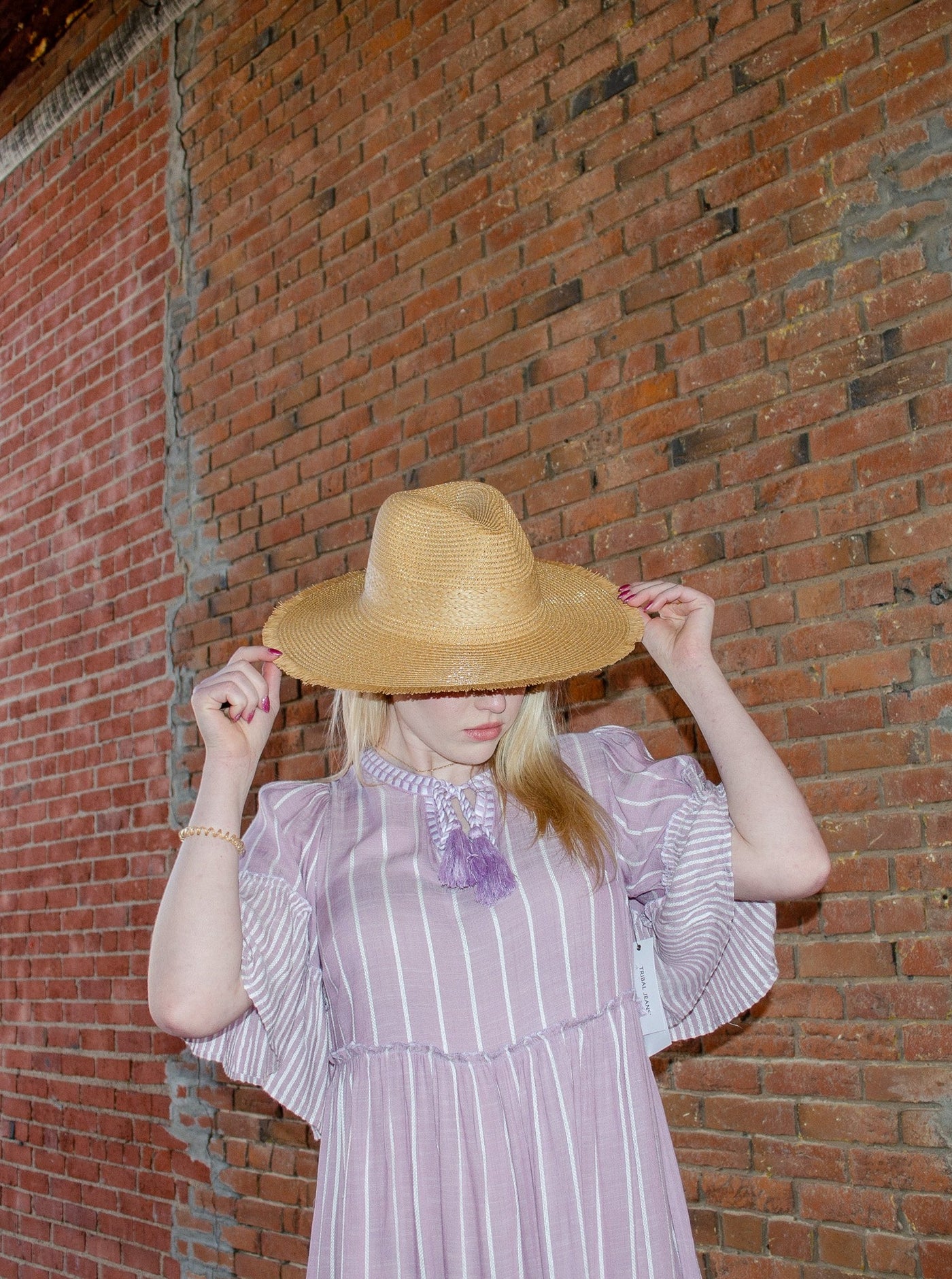 Model is wearing a wide brimmed straw sunhat. Hat is the color light brown.