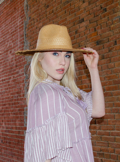 Model is wearing a wide brimmed straw sunhat. Hat is the color light brown.