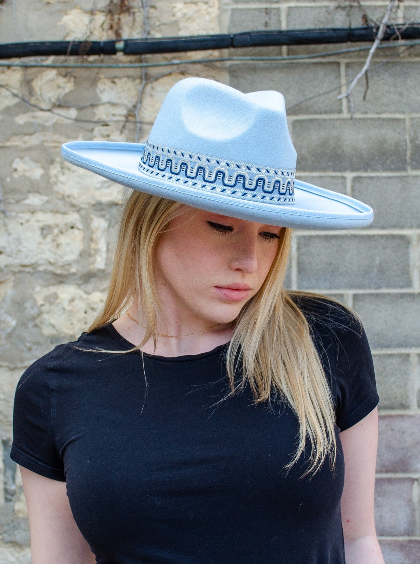 Model is wearing a boho style baby blue flat brim hat with a boho printed strap on the base of hat.