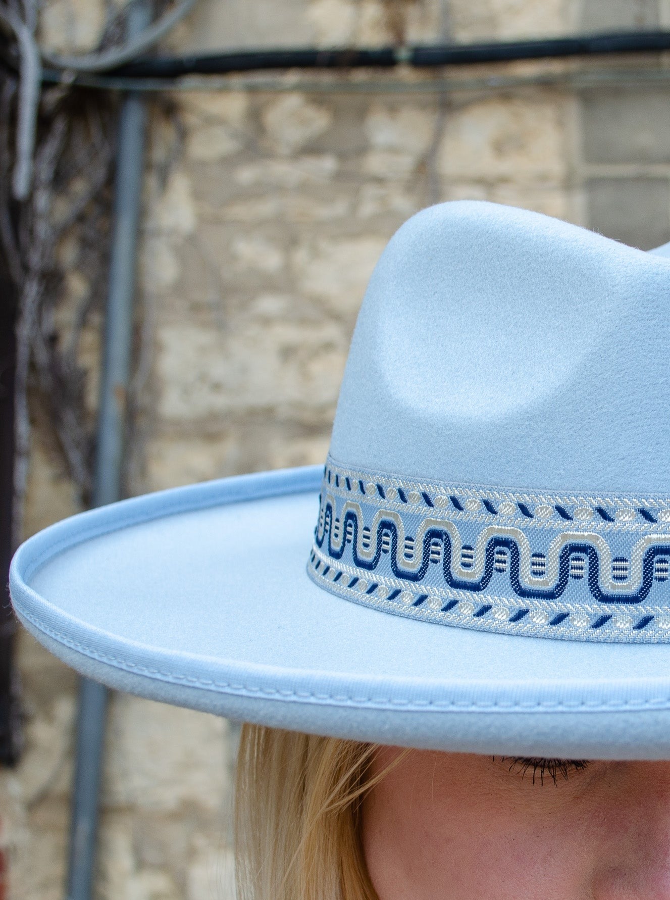 Model is wearing a boho style baby blue flat brim hat with a boho printed strap on the base of hat.