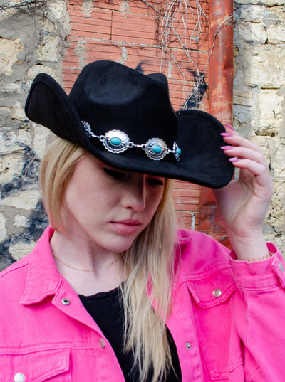Model is wearing a black cowboy hat with turquoise and silver jewel detail. 