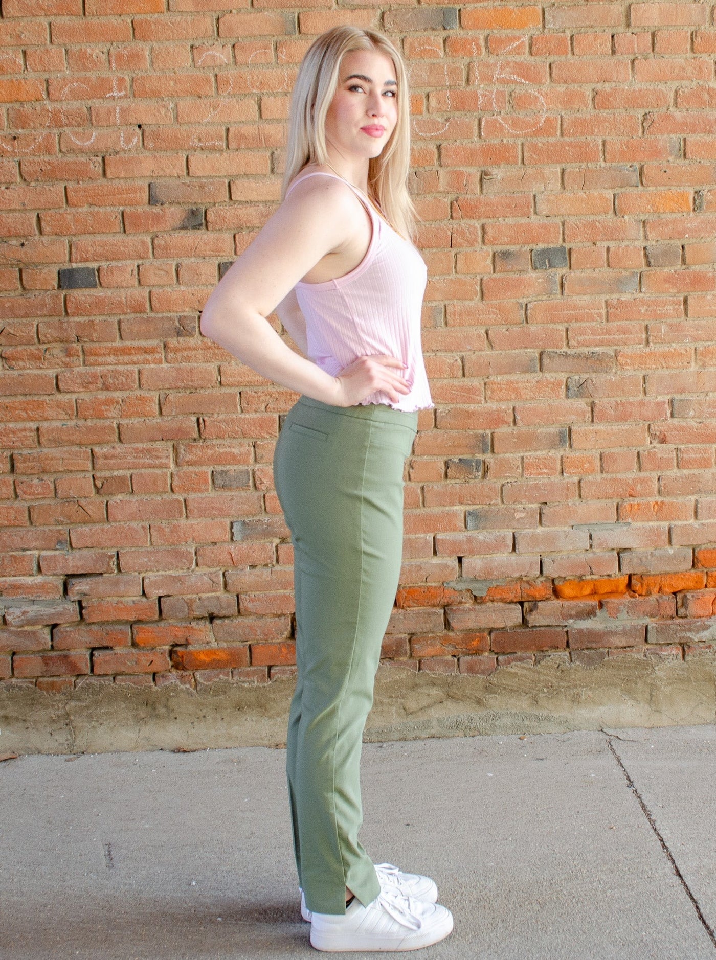 Model is wearing a sage green cigarette style pull on pant. Pants are paired with a tank top and sweater. 