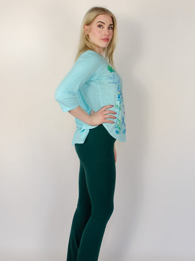 Model is wearing a baby aqua blue tunic top with floral print on the front. 