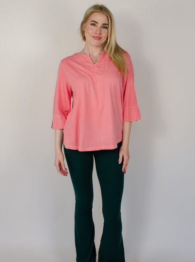 Model is wearing a salmon colored 3/4th sleeve top with a v-neck neckline. Top is worn with teal leggings.