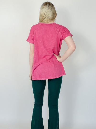 Model is wearing a pink oversized T shirt with floral designs and pockets in the front. 