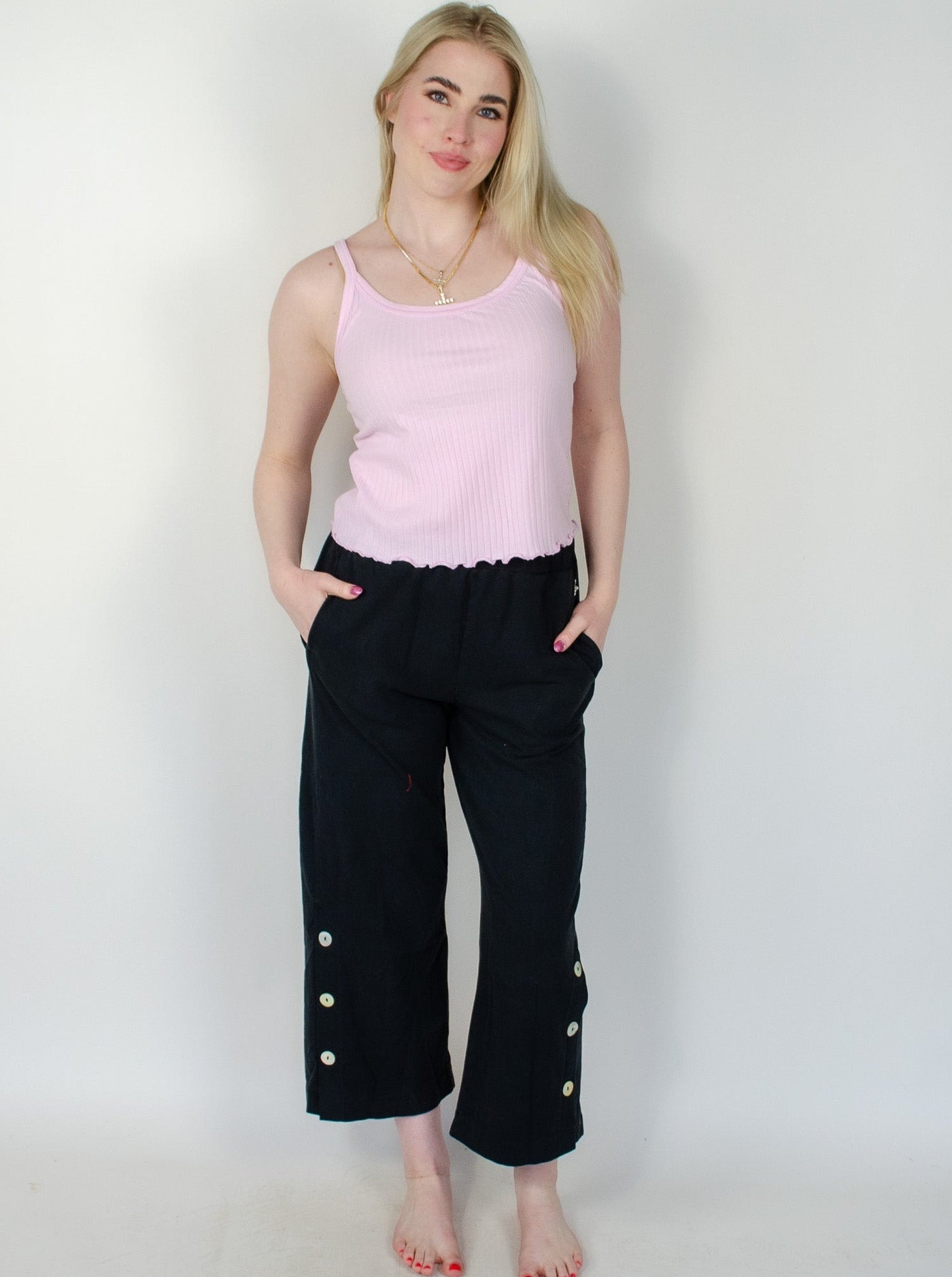 Model is wearing a black low rise sweatpant with slits on the outside of ankle with button details. 