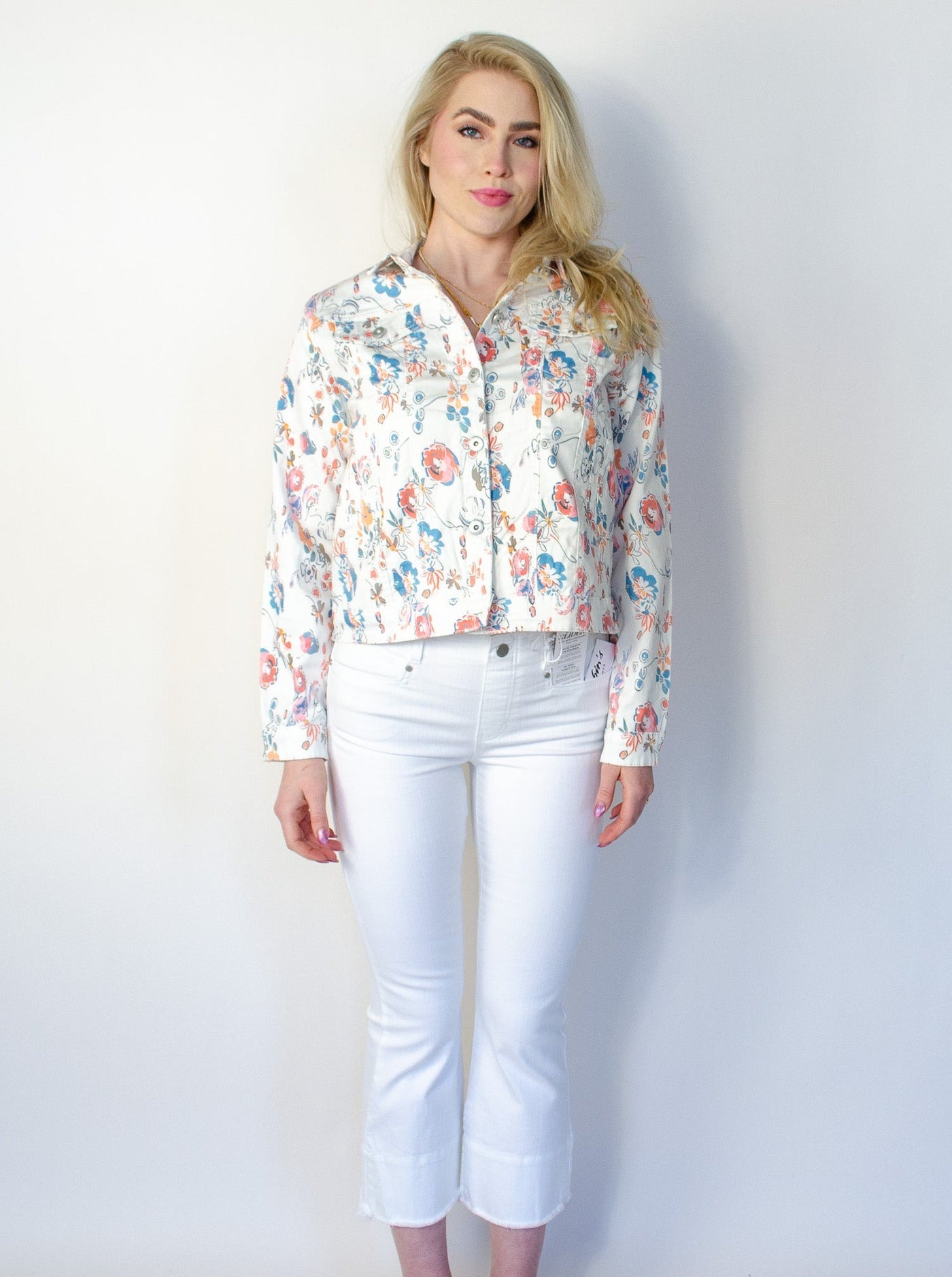 Model is wearing a white denim jean jacket with floral printed detail. Jean jacket is worn with white jeans.