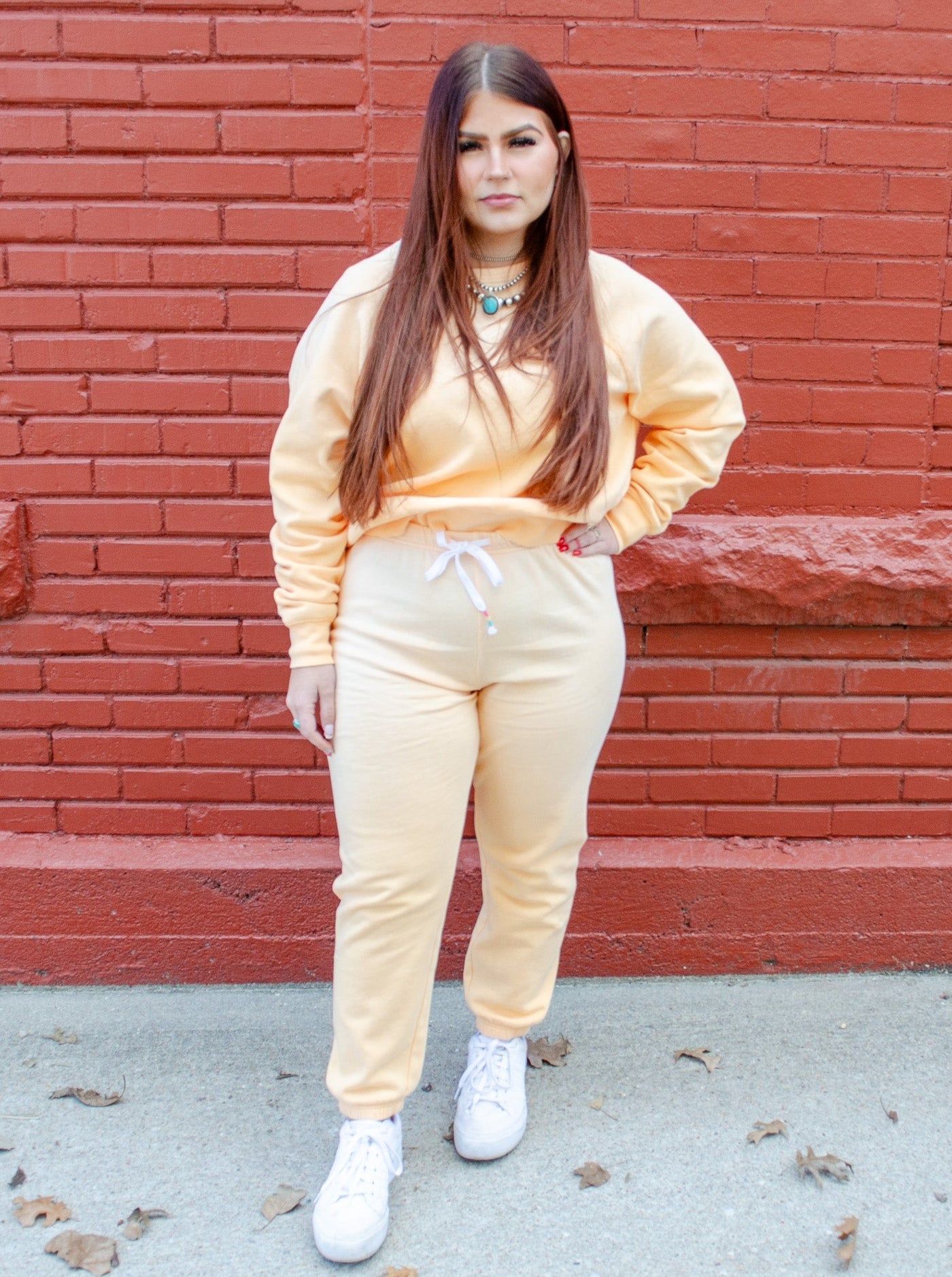 Model is wearing an orange cream colored jogger paired with a matching sweatshirt. Joggers have rainbow details on the drawstrings.  