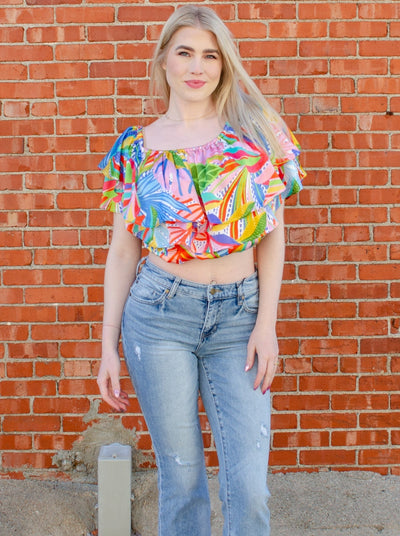 Model is wearing a tropical printed ruffled crop top. Top is worn with blue jeans. 