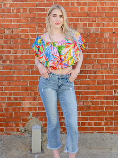 Model is wearing a cropped light wash denim jean with frayed hemming at the ankle. Jeans are worn with a flowy blouse.