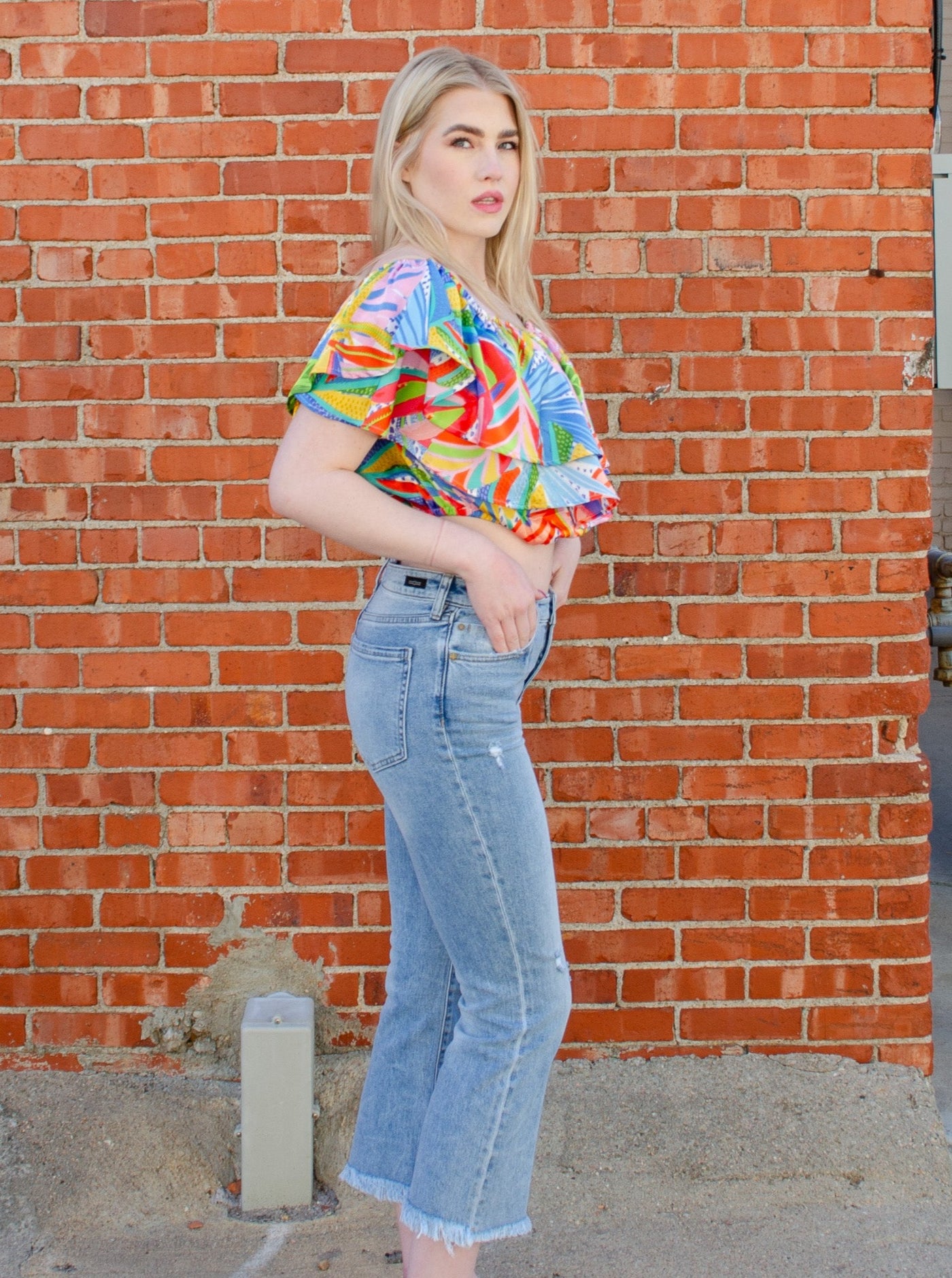 Model is wearing a cropped light wash denim jean with frayed hemming at the ankle. 