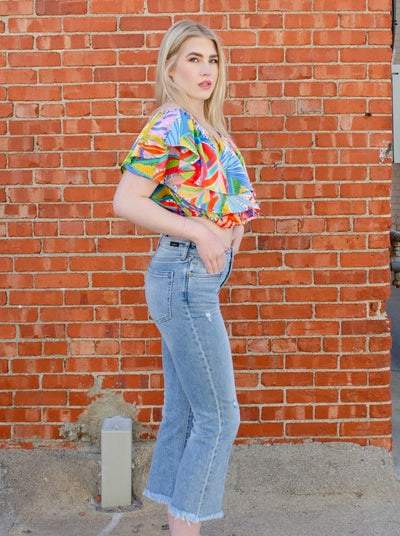 Model is wearing a cropped light wash denim jean with frayed hemming at the ankle. 