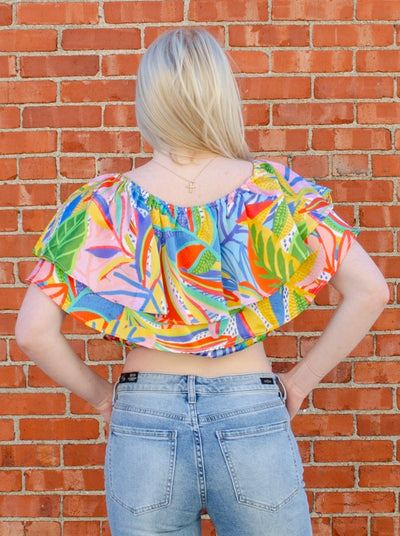 Model is wearing a tropical printed ruffled crop top. Top is worn with blue jeans.