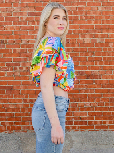 Model is wearing a tropical printed ruffled crop top. Top is worn with blue jeans.