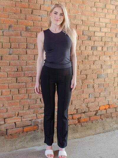 Model is wearing black flare yoga pants with a pleat down the middle of each leg. Yoga pants are paired with a black tank top. 