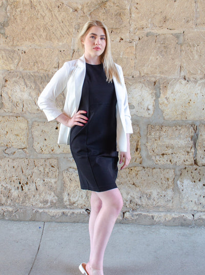 Model is wearing a black professional style midi dress. Worn with a white blazer. 