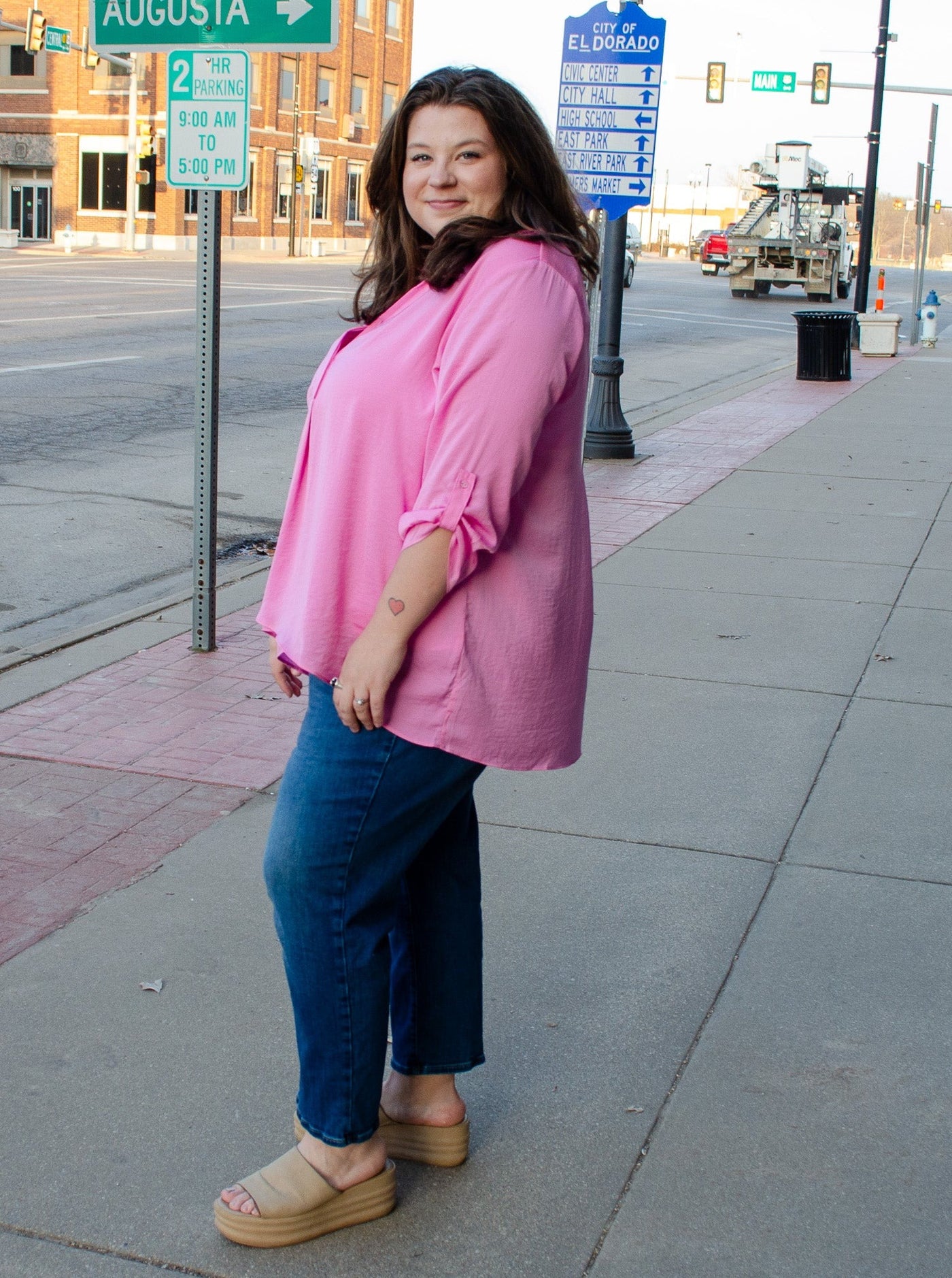 A model wearing a light pink airflow blouse pinned up sleeves and a v-neckline with collar. She has it paired with dark wash jeans.