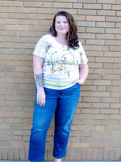 Model is wearing a linen green and yellow accented floral top paired with blue jeans.