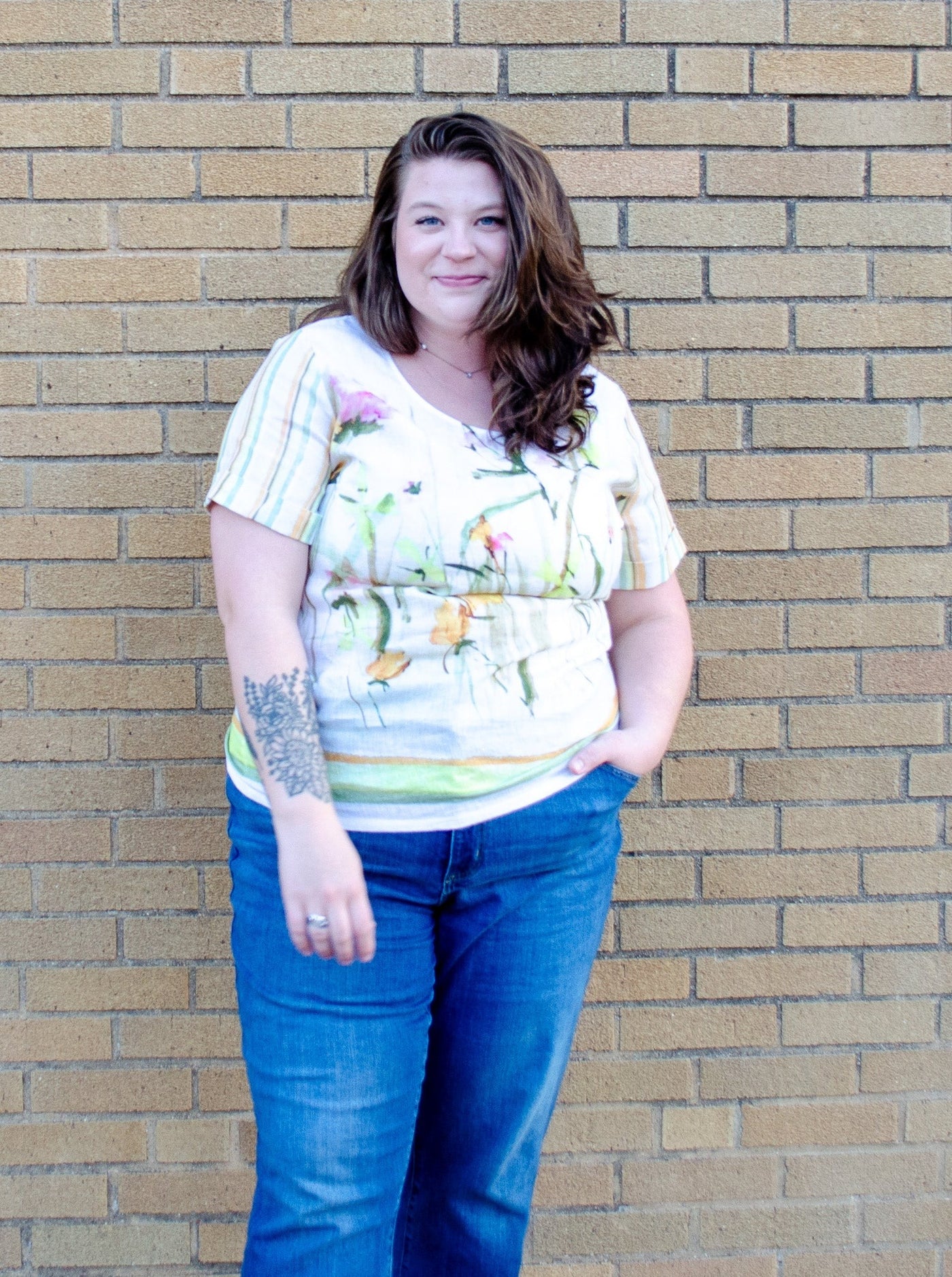 Model is wearing a linen green and yellow accented floral top paired with blue jeans.