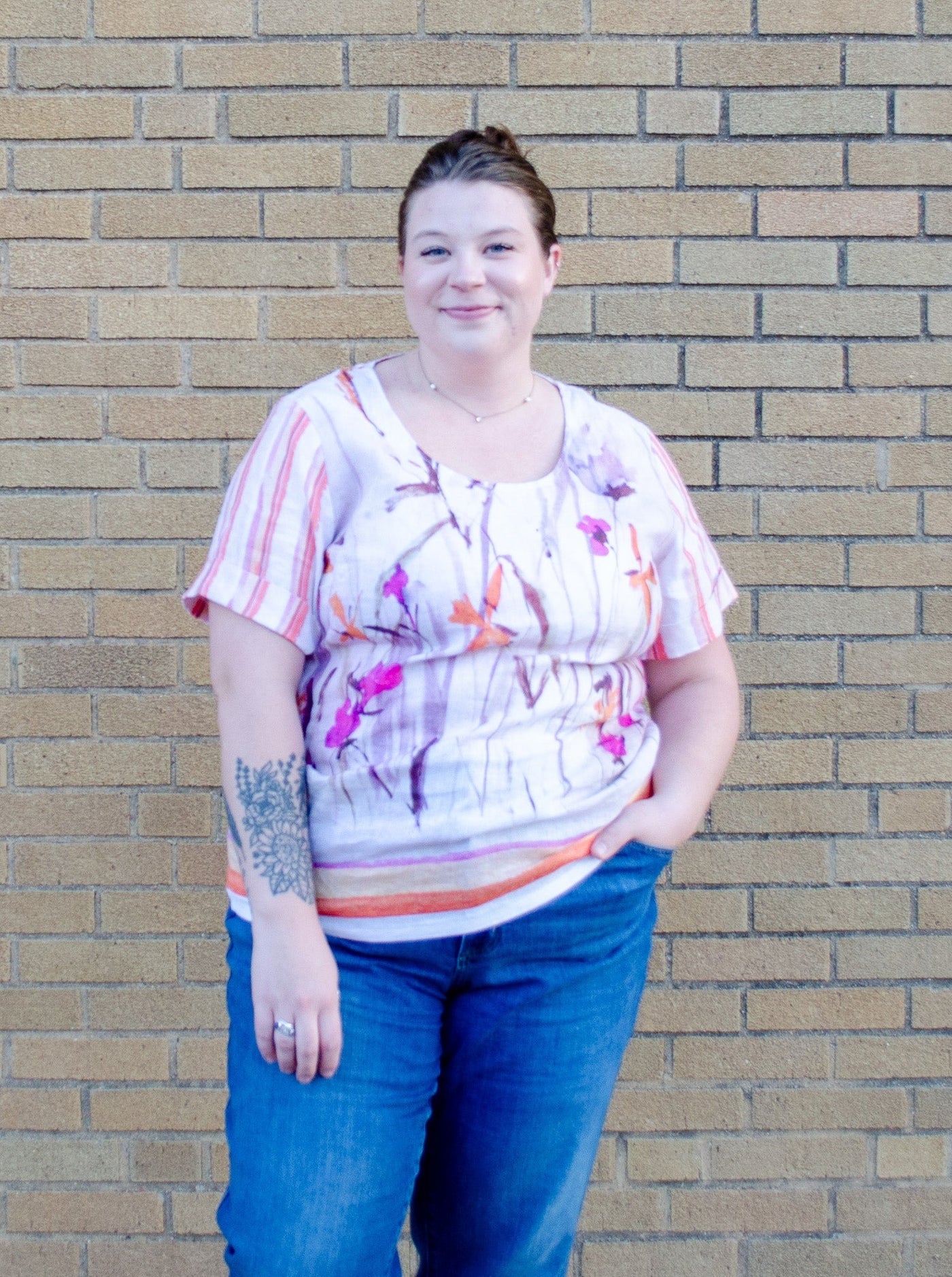 Model is wearing a linen pink and orange accented floral top paired with blue jeans.