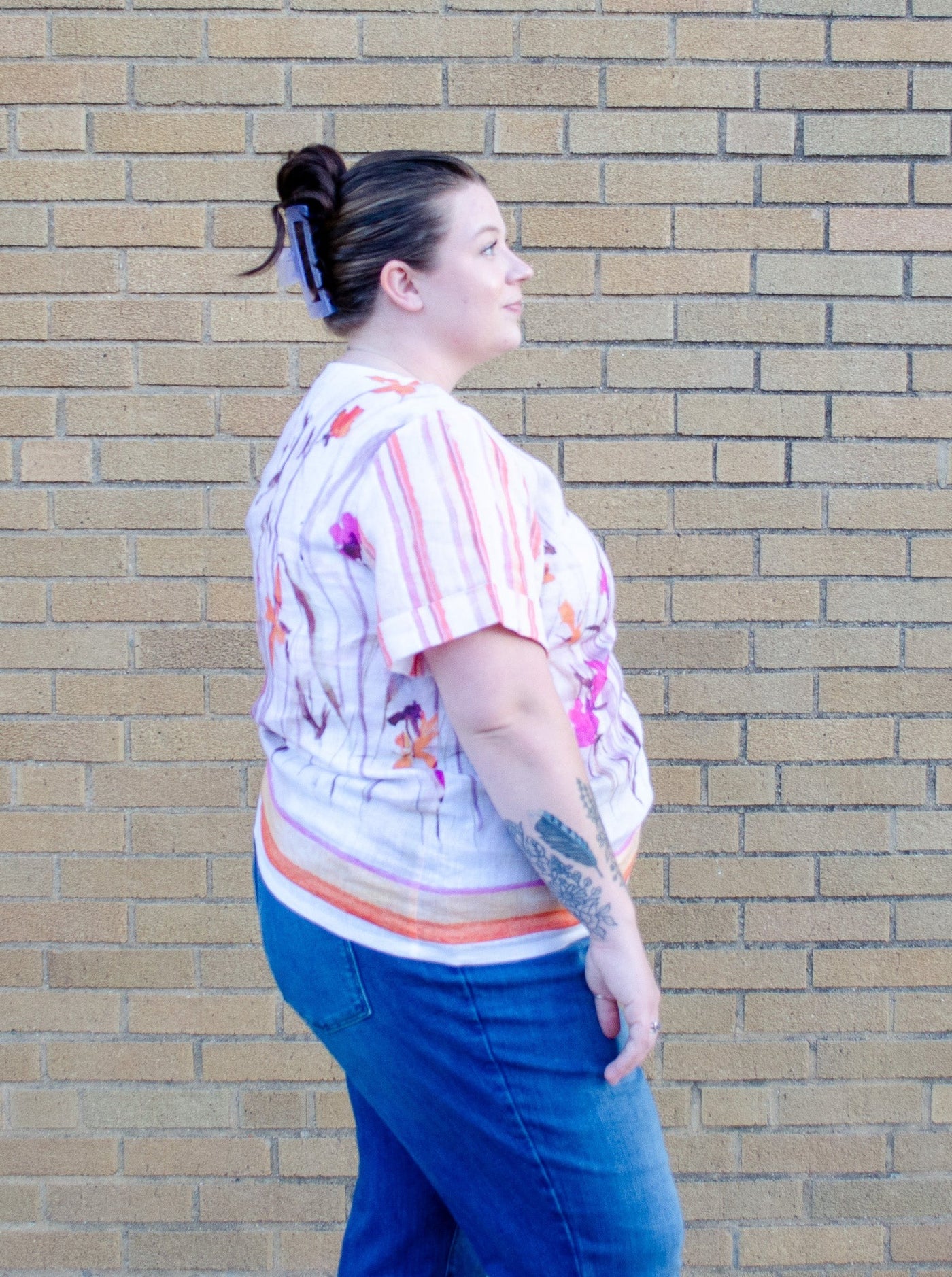 Model is wearing a linen pink and orange accented floral top paired with blue jeans.