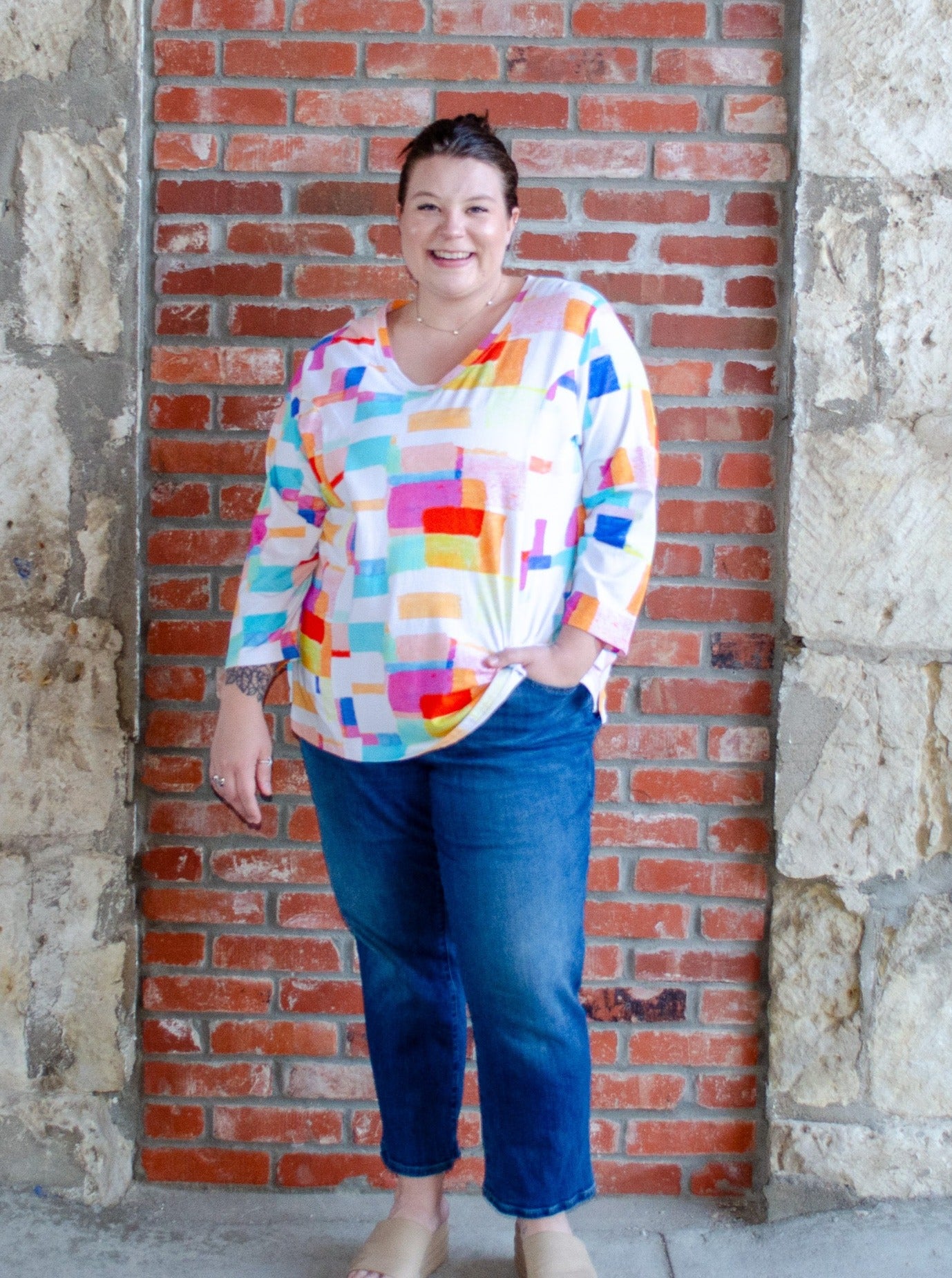 Model is wearing a V-neck style white long sleeve with multi color block print. Worn with dark wash blue jeans.