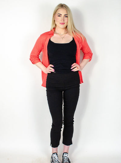 Model is wearing a black ankle pull on pant with small slits at the ankles. Pant is worn with a tank top and salmon colored button up.