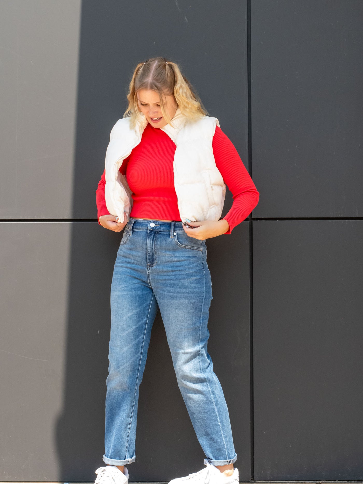 A model wearing a cream, cropped puffer vest. The model has it paired with a read mock neck underneath and light wash jeans.