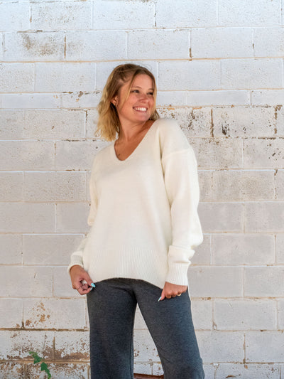 A model wearing a cream v-neck sweater. She has it paired with a pair of wide leg gray pants.
