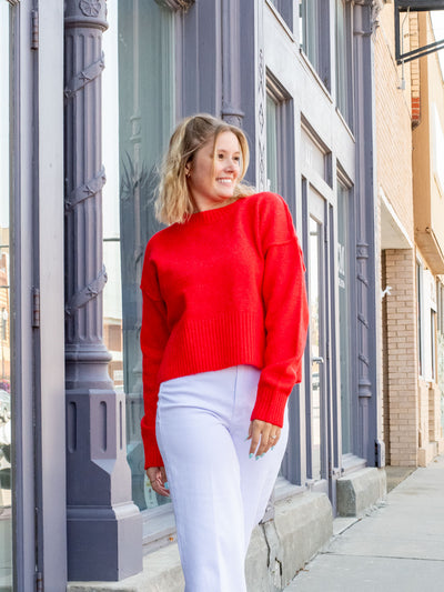 A model wearing a red sweater with hem and sleeve details and side slits. She has it paired with white jeans.