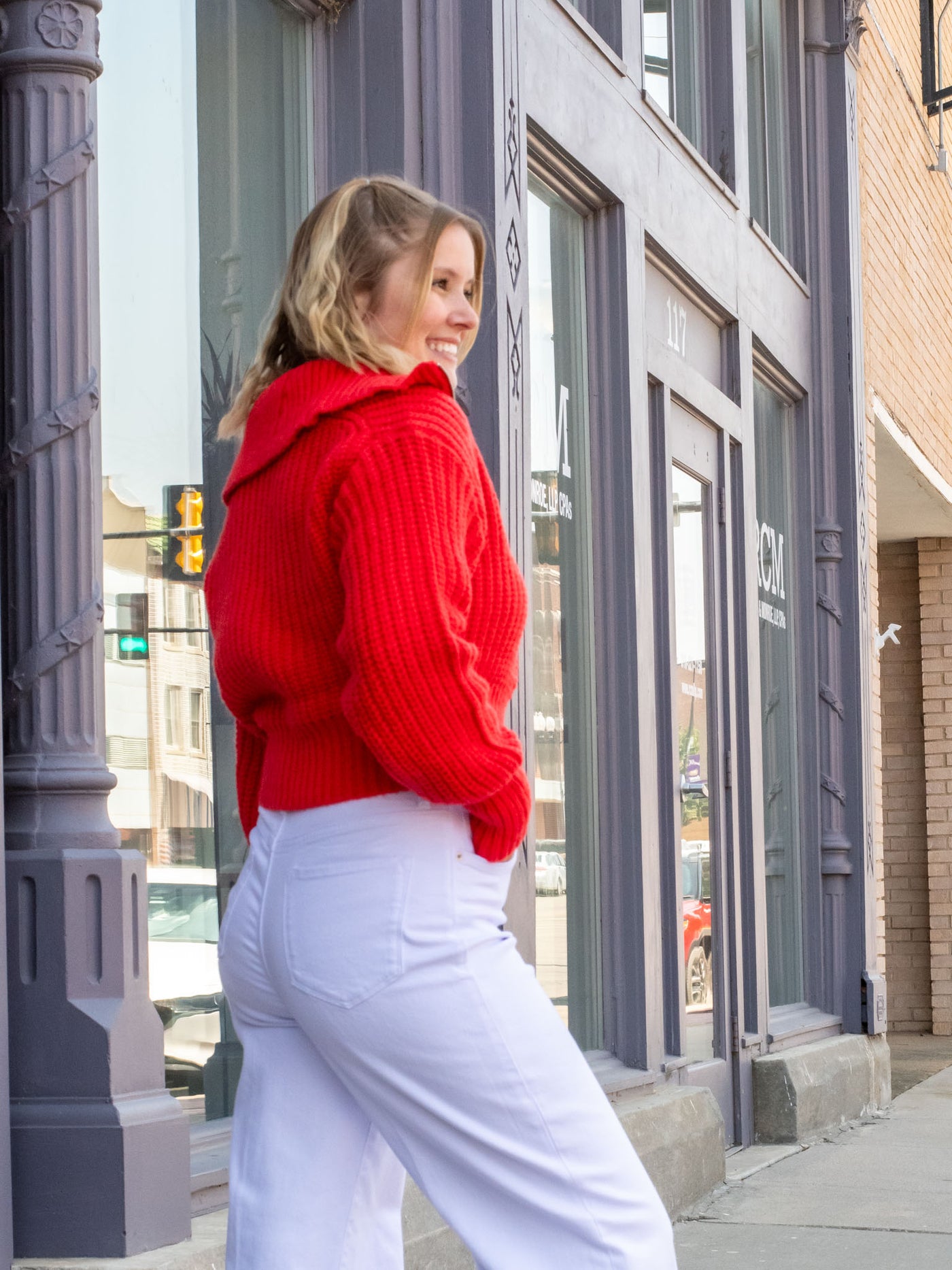 A model wearing a cropped red two-way zip sweater with a large collar. She has it paired with white jeans. 