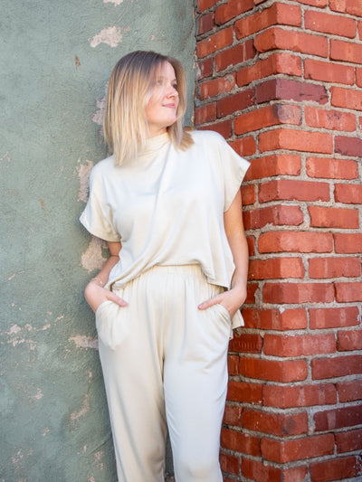 A model wearing an off white jumpsuit with an attached front, detached back, and a jogger pant.