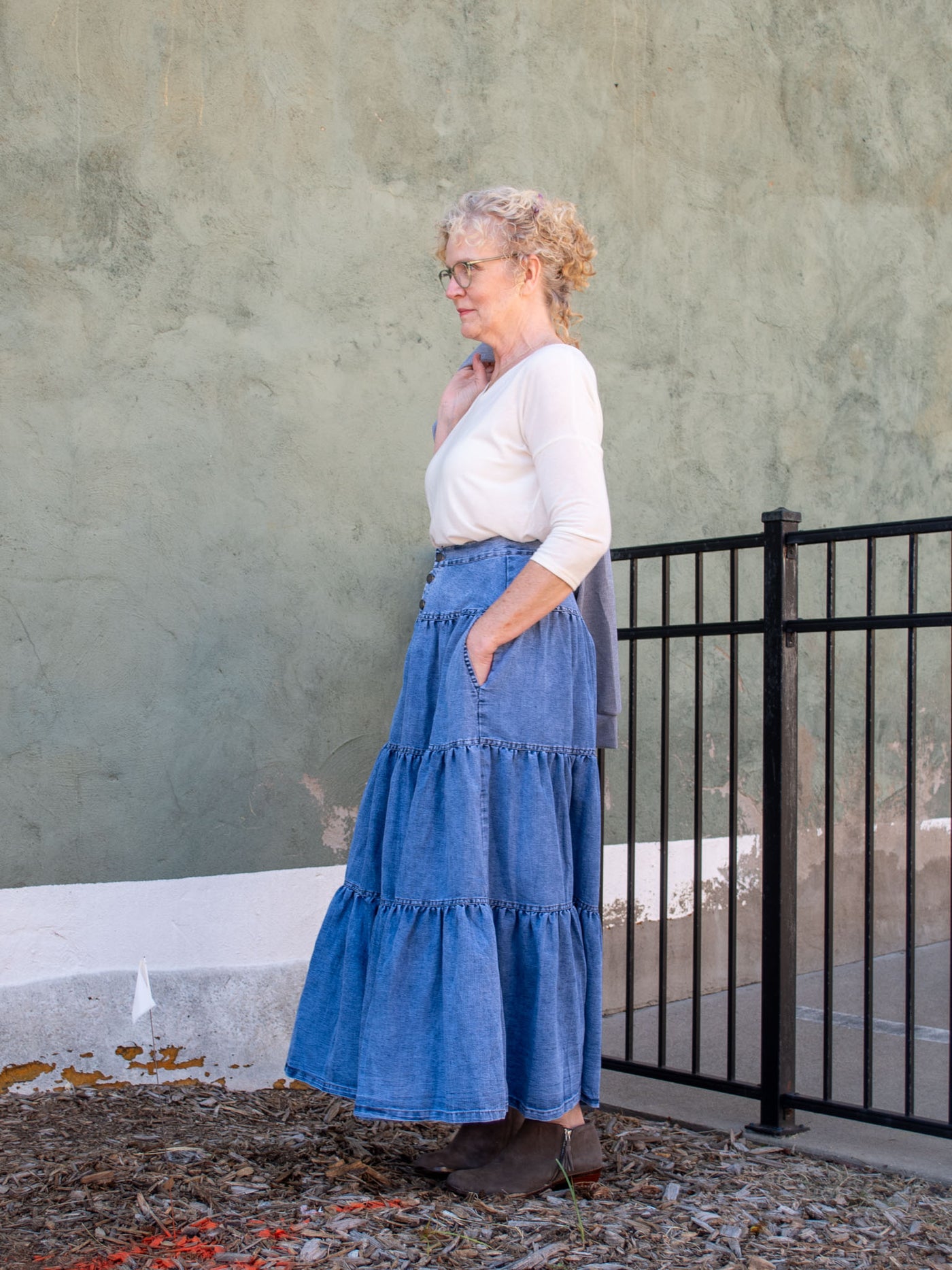 A model wearing a denim tiered maxi skirt. The model has it paired with an off white top and gray booties.