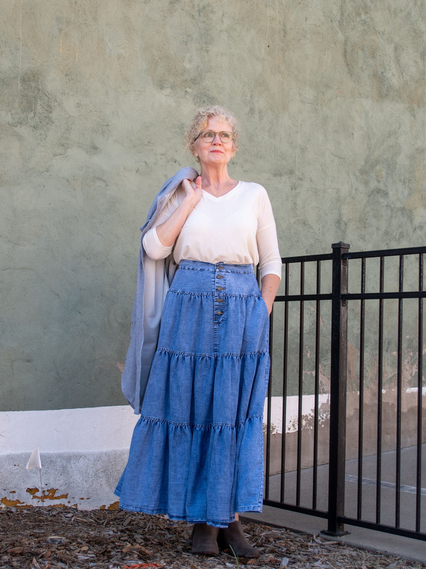 A model wearing a denim tiered maxi skirt. The model has it paired with an off white top and gray booties.
