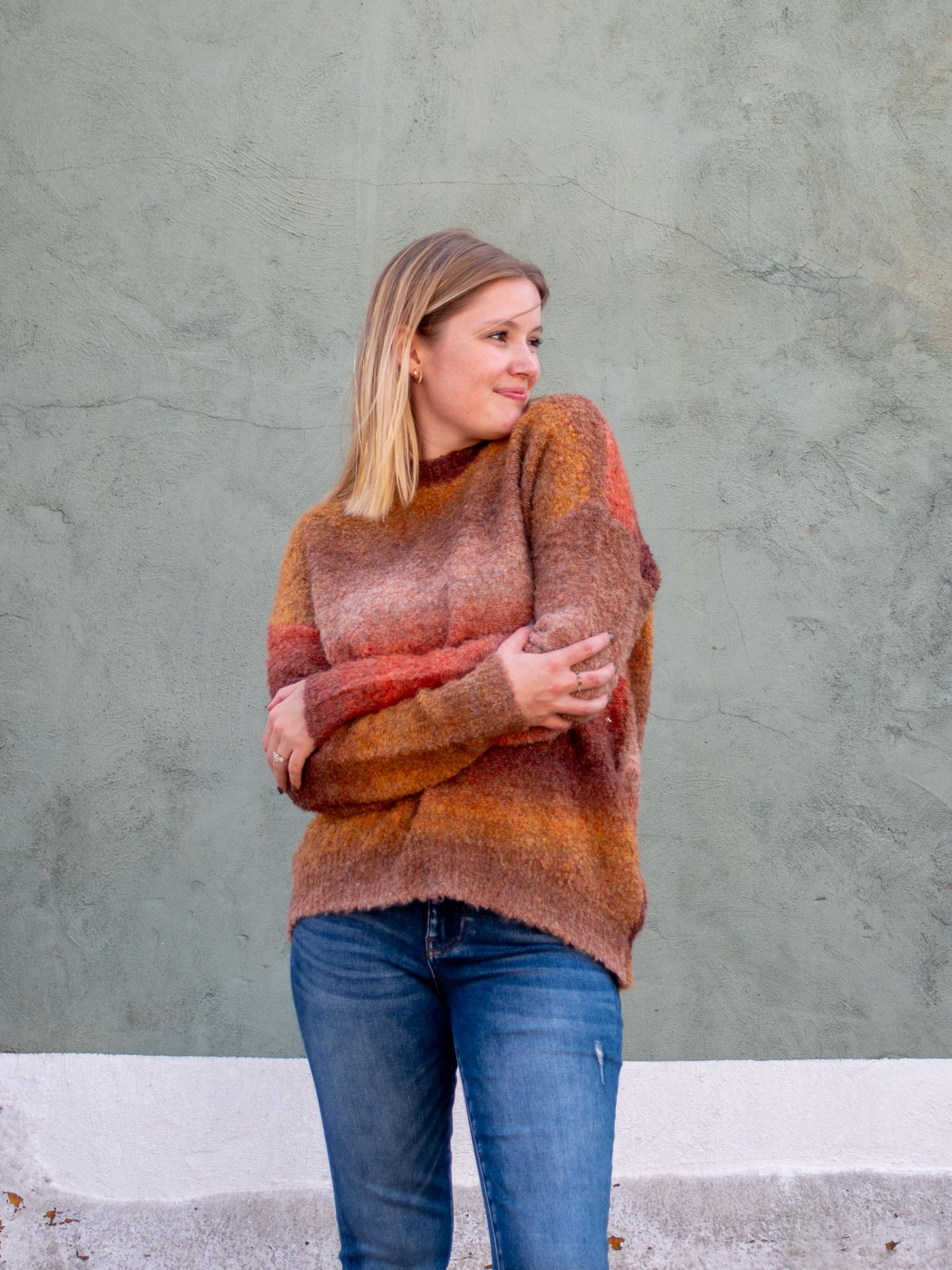 A model wearing a fall brown, rush, and tan crewneck sweater. The model has it paired with a medium wash jean.