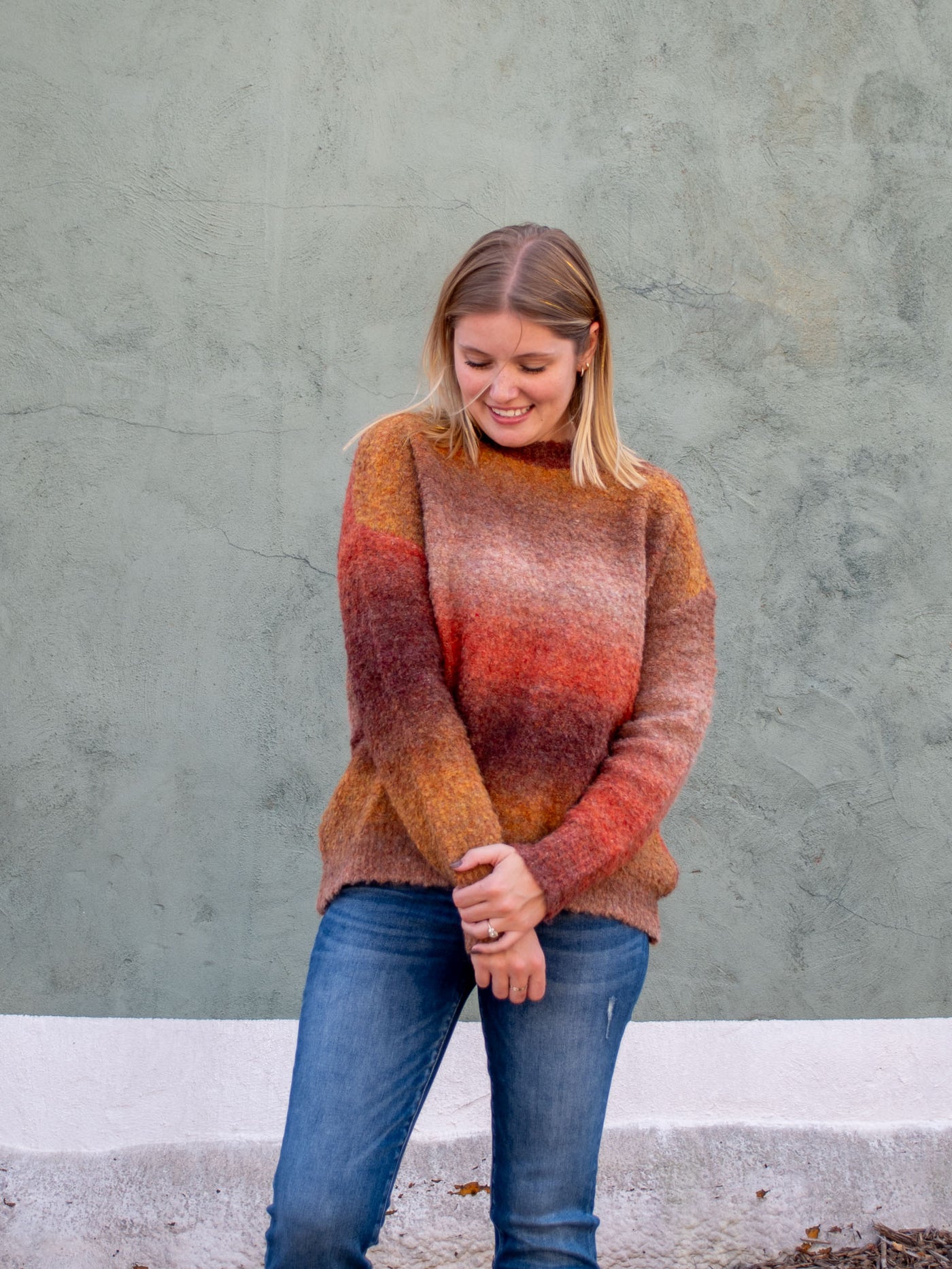 A model wearing a fall brown, rush, and tan crewneck sweater. The model has it paired with a medium wash jean.