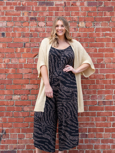 A model wearing a tan colored oversized chunky cardigan. The model has it paired over a black animal print jumpsuit. 