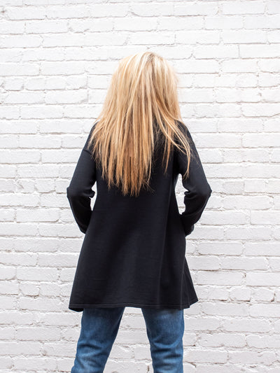 A model wearing a long black sweater top with sparkle around the top. The model has it paired with a medium wash jean.