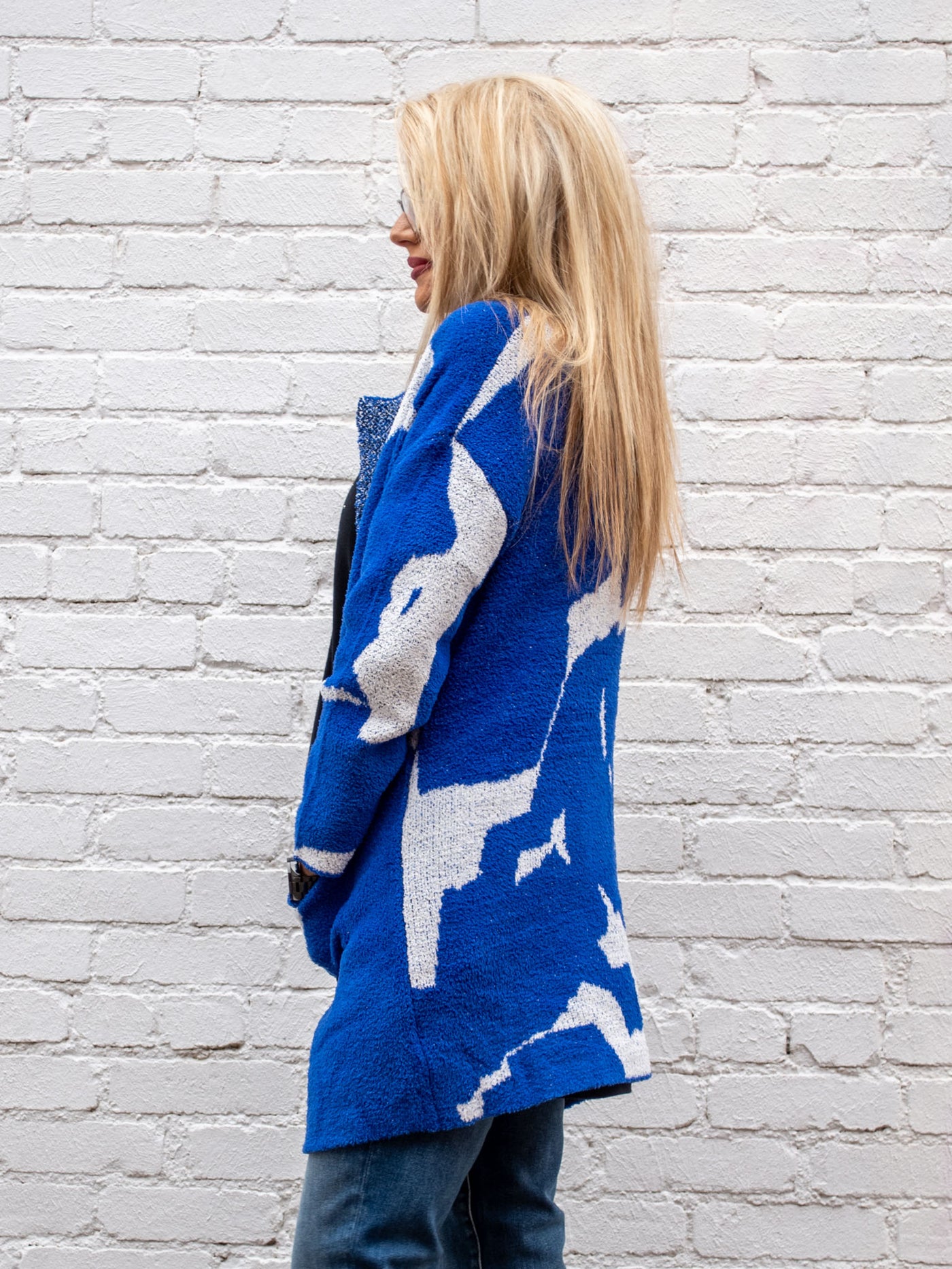A model wearing a blue, white and black printed cardigan. The model has it paired over a medium wash jean and black top.