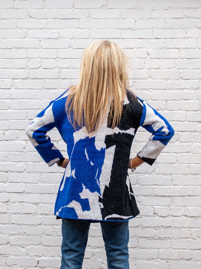 A model wearing a blue, white and black printed cardigan. The model has it paired over a medium wash jean and black top.