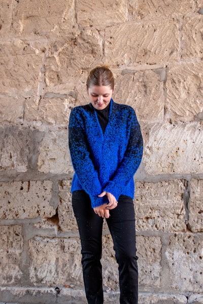 A model wearing a blue and black fuzzy open front cardigan. The model has it over a black mock neck and black jeans.
