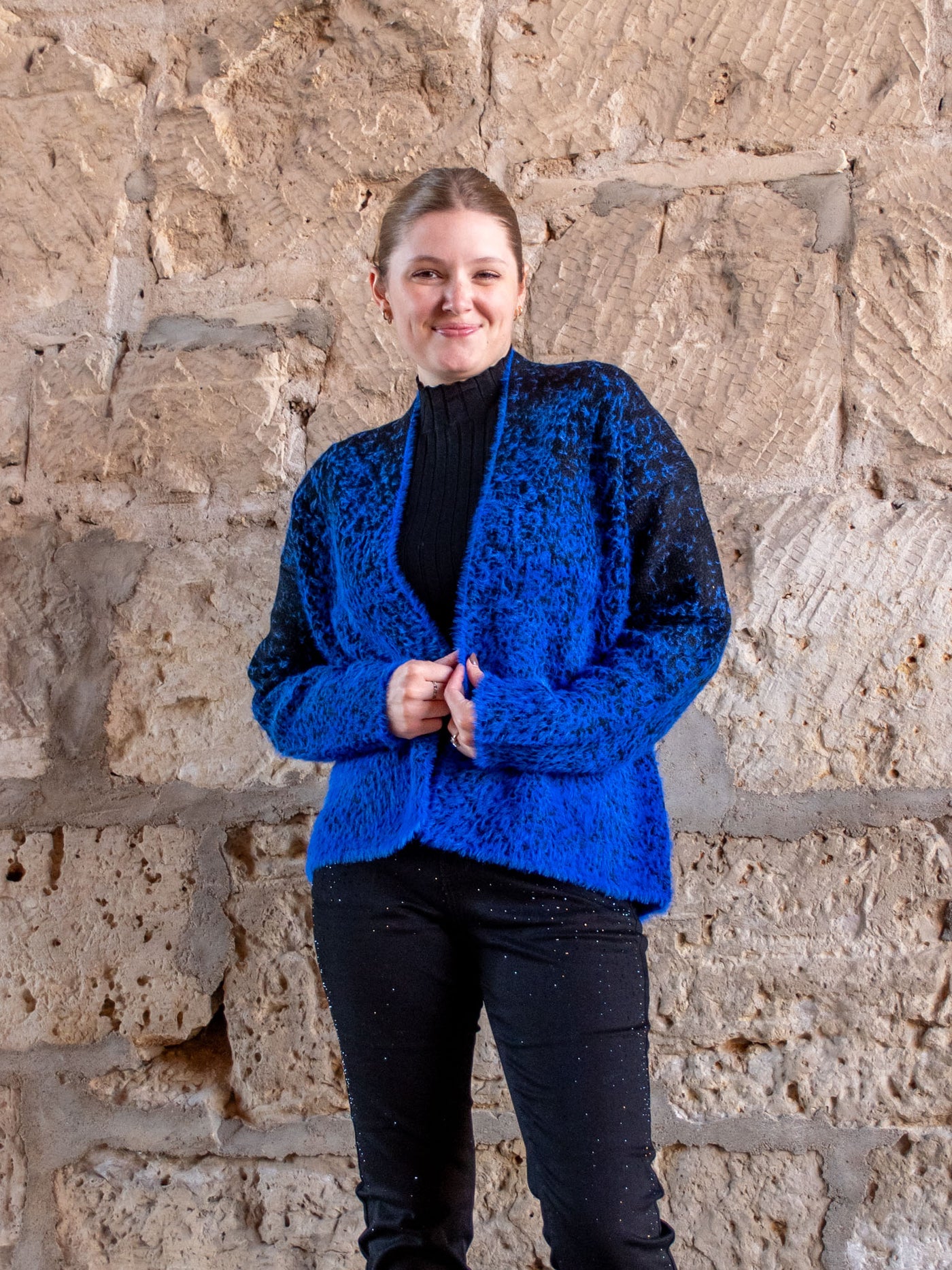 A model wearing a blue and black fuzzy open front cardigan. The model has it over a black mock neck and black jeans.