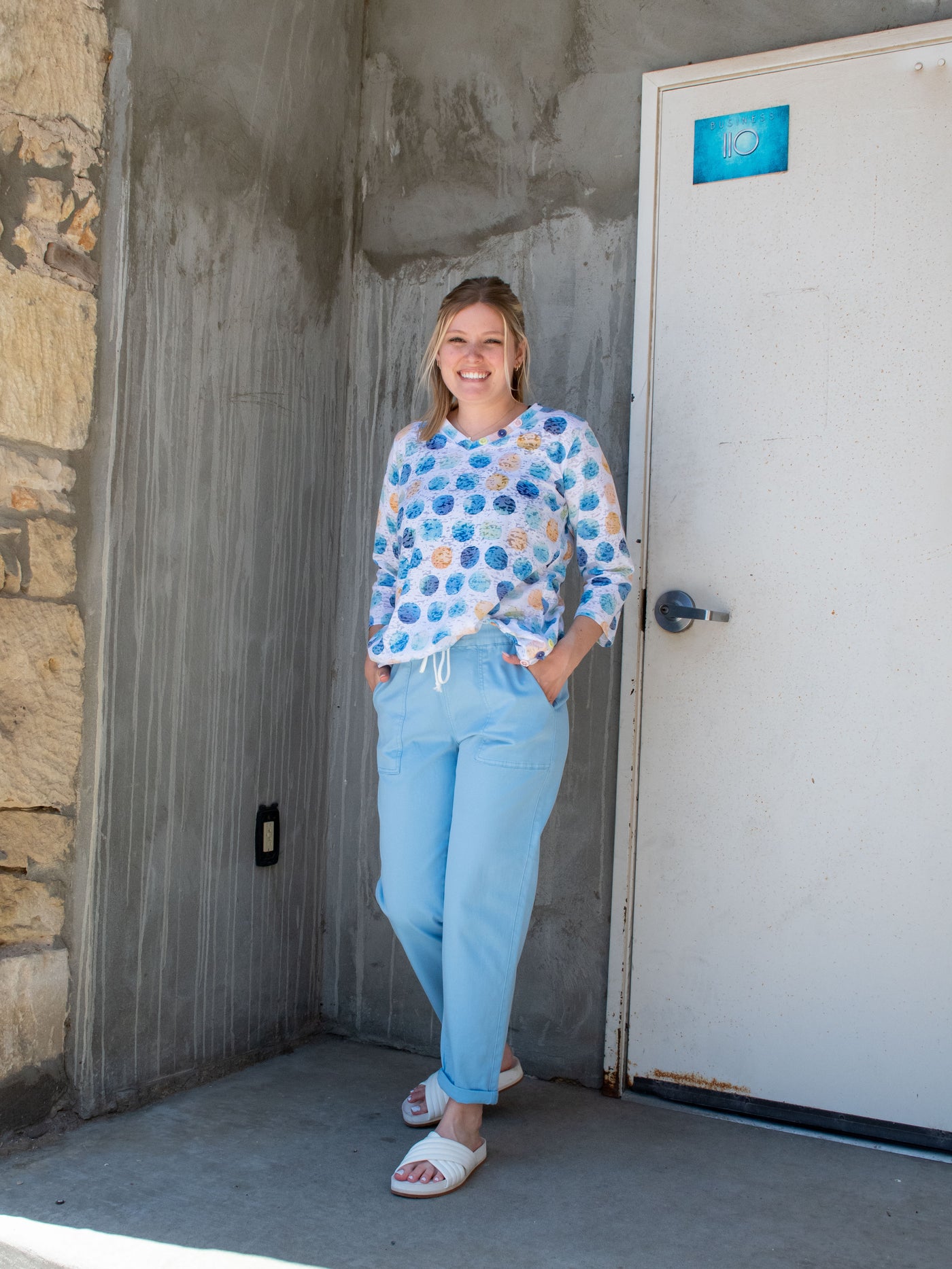 A model wearing a pair of blue faux denim joggers with a polka dot top and white slide sandals.