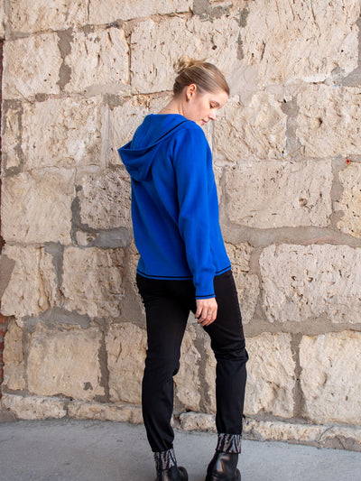A model wearing a royal blue button up sweater with a hood. The model has it paired with a black rhinestone jean.