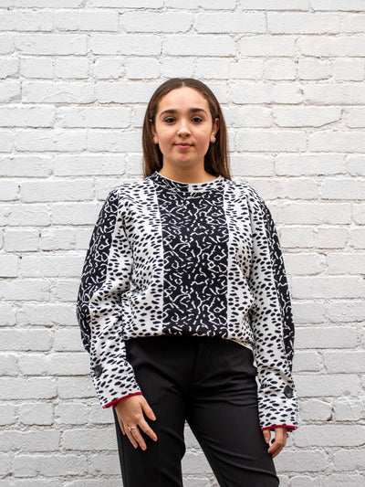 A model wearing a black and white color blocked top with an all over animal print pattern. The model has it paired with a black trouser.